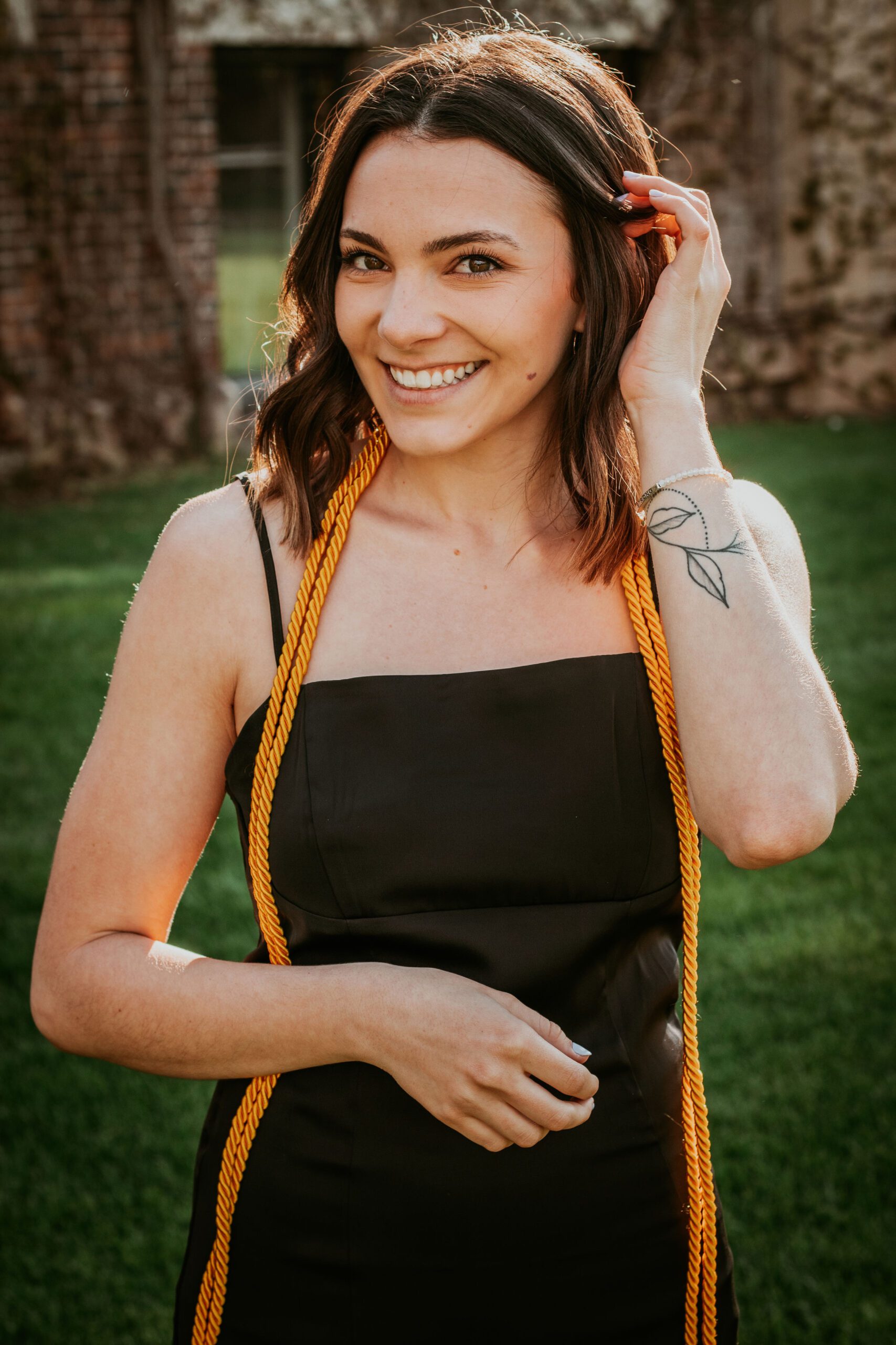 Alexa smiles at the camera while tucking her hair behind her ear on graduation day