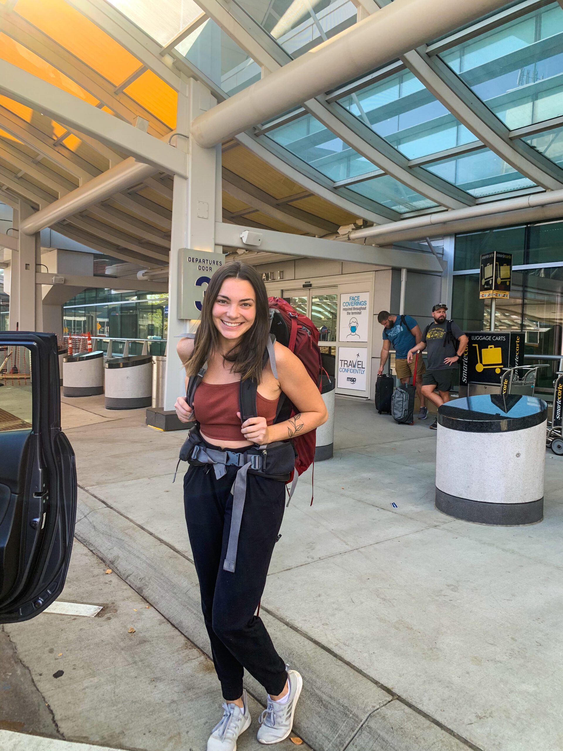 Alexa stands in front of the airport entrance with her backpack before leaving on her first solo backpacking trip