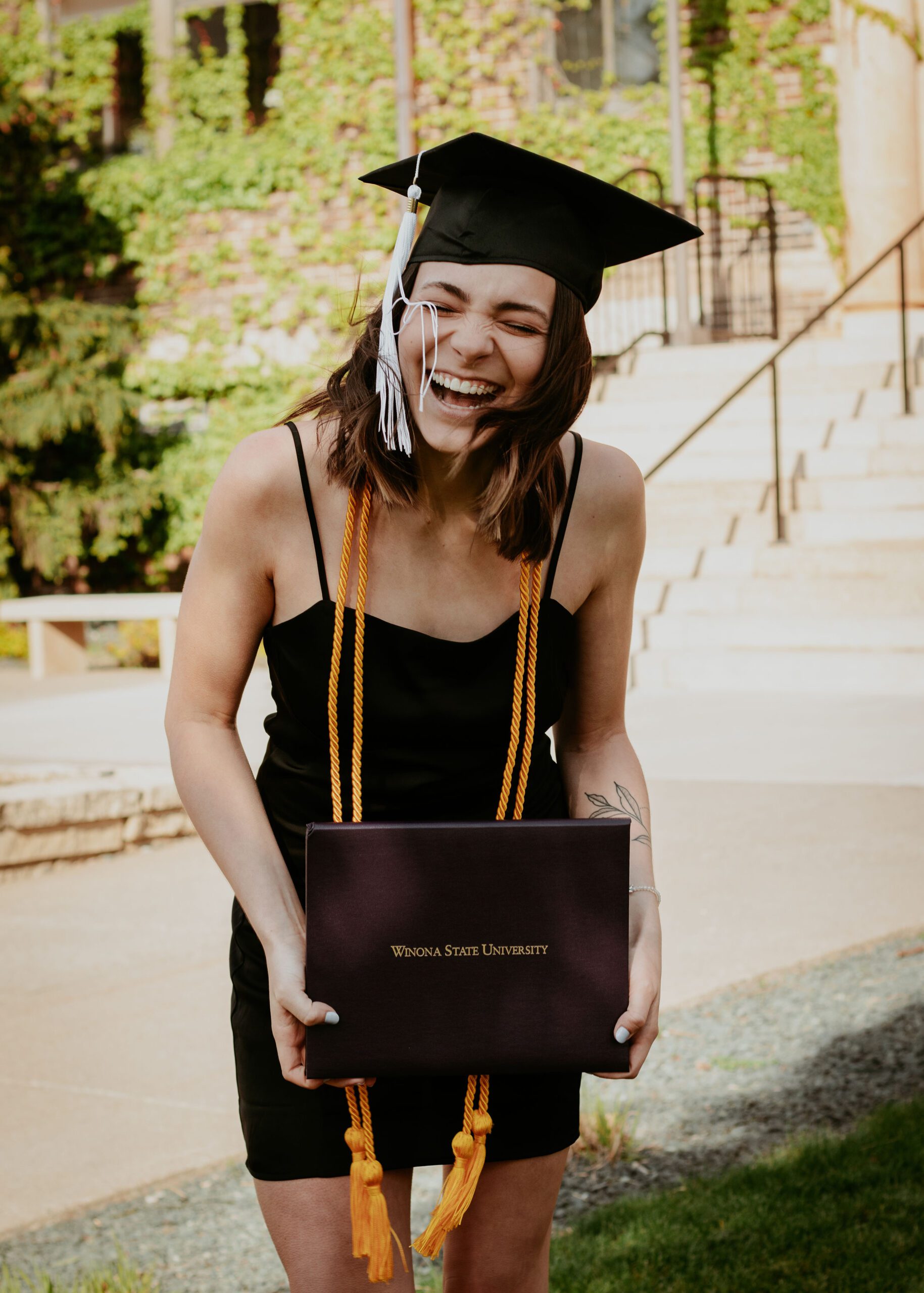 Alexa is laughing on a windy day while holding her college diploma