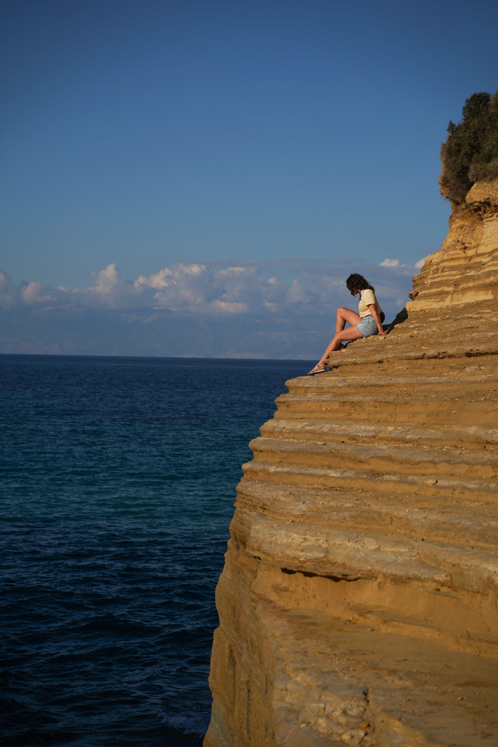 Alexa sits on the edge of a cliff over the ocean at Canal'D'Amour