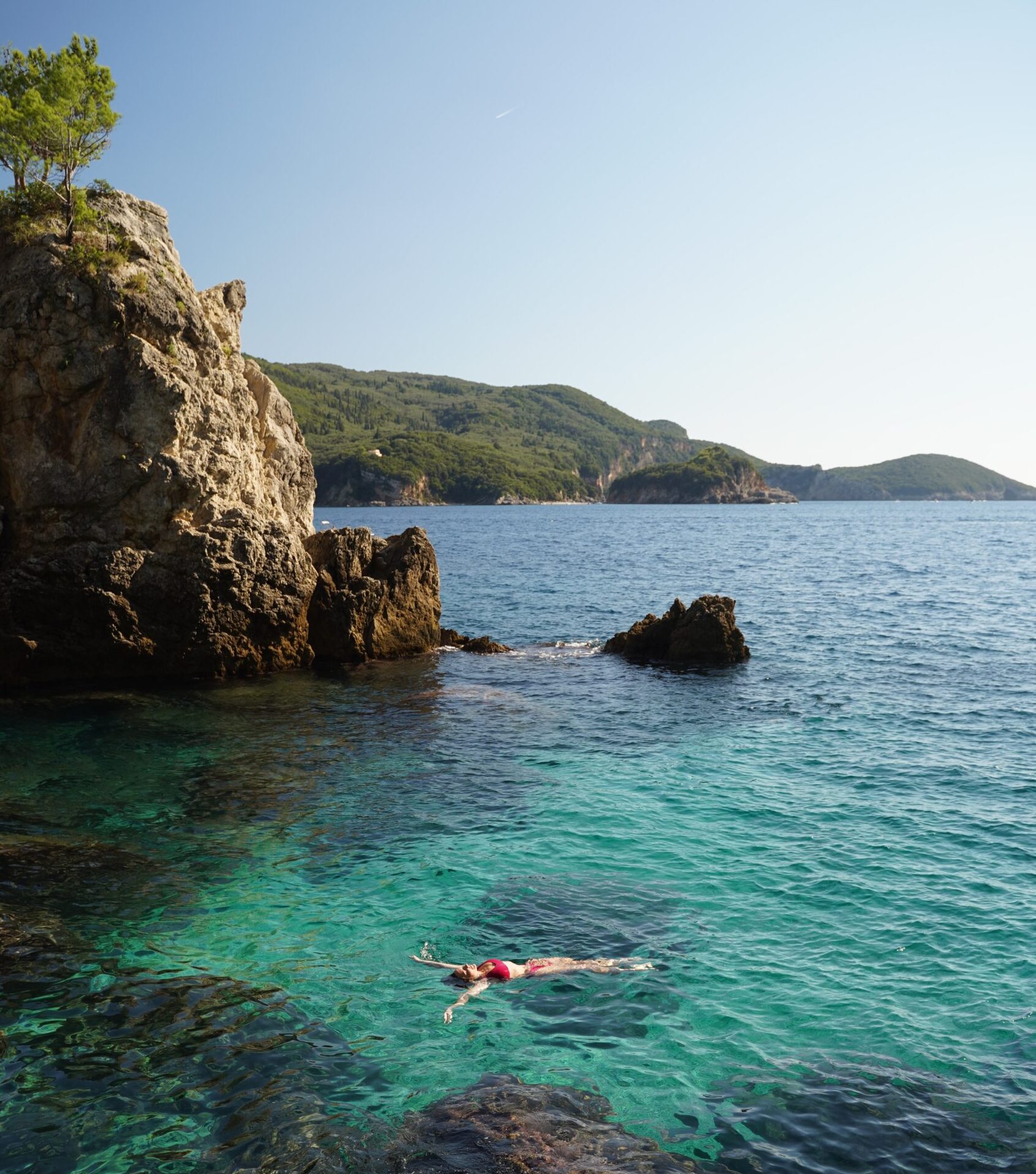 A person is swimming in the ocean near a rocky cliff.