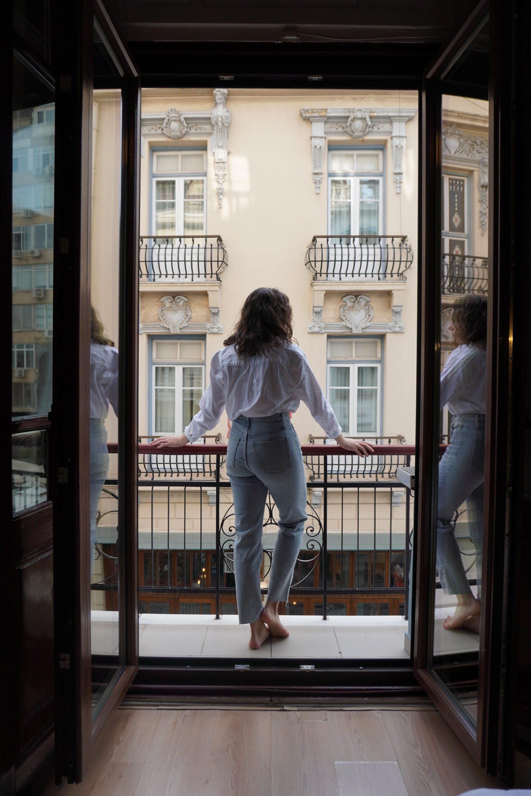 A woman on her first solo backpacking trip, standing on a balcony and looking out of an open door.