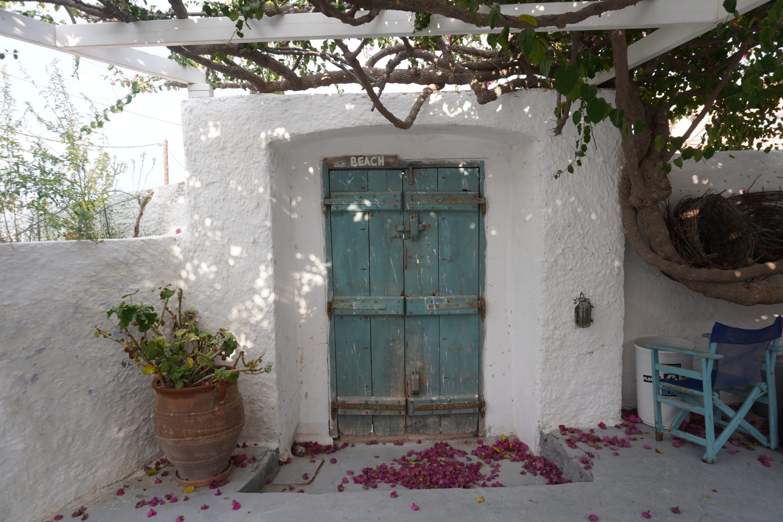 A blue door with an arrow sign that reads "beach" surrounded by white walls in Santorini, Greece