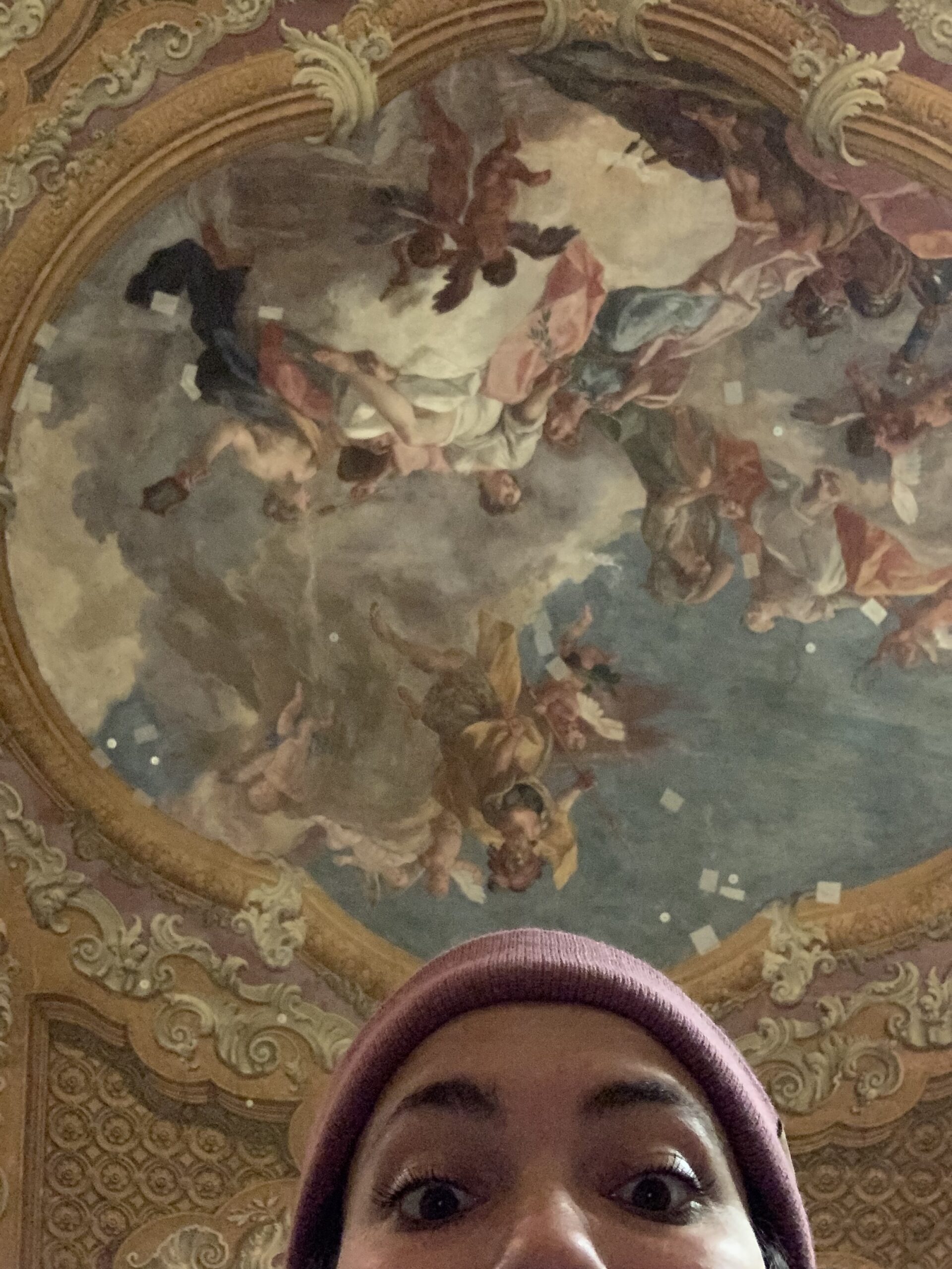 A woman capturing a selfie in front of an exquisite ceiling.