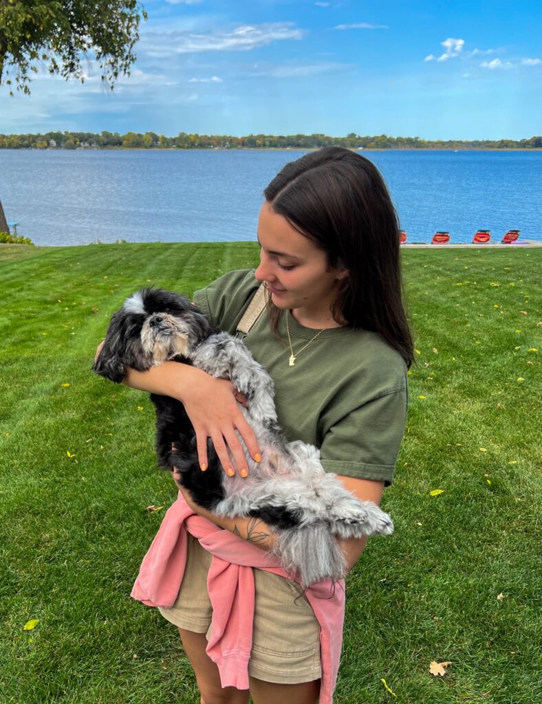 A woman holding a dog in front of a serene lake.