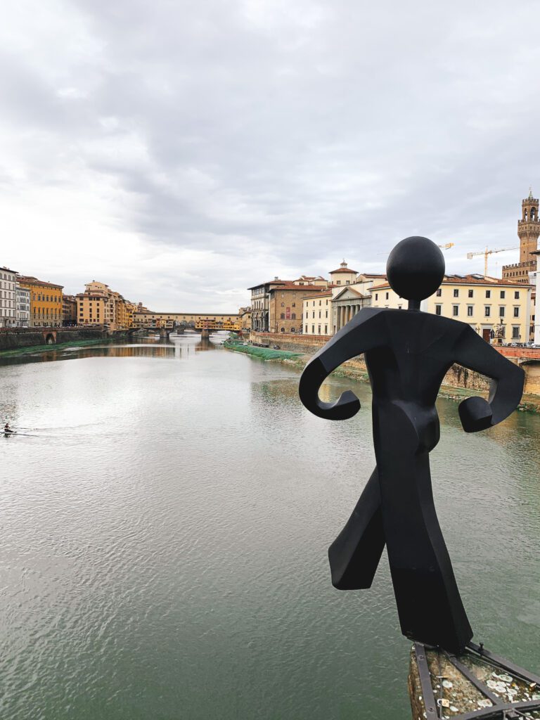 A man struggling with imposter syndrome stands on a bridge over a tranquil river.