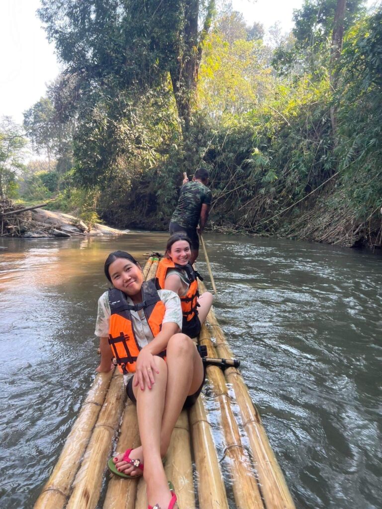 Two individuals enjoying a serene journey down the river on a bamboo raft.