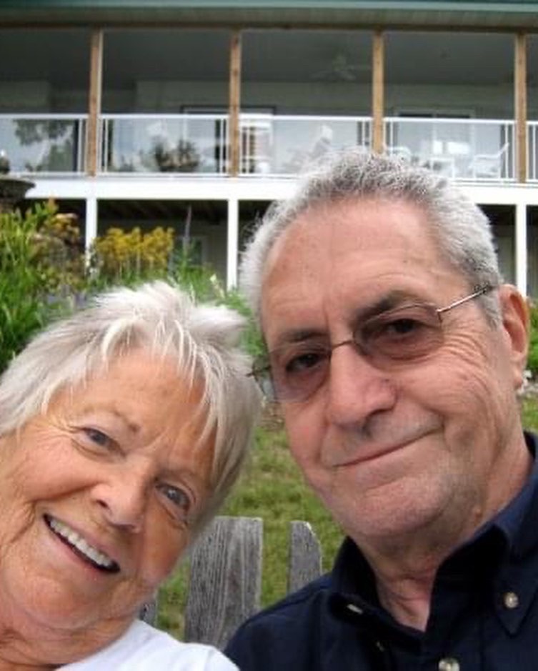 An older couple, Ronnie & Barbie smiling in front of a house.