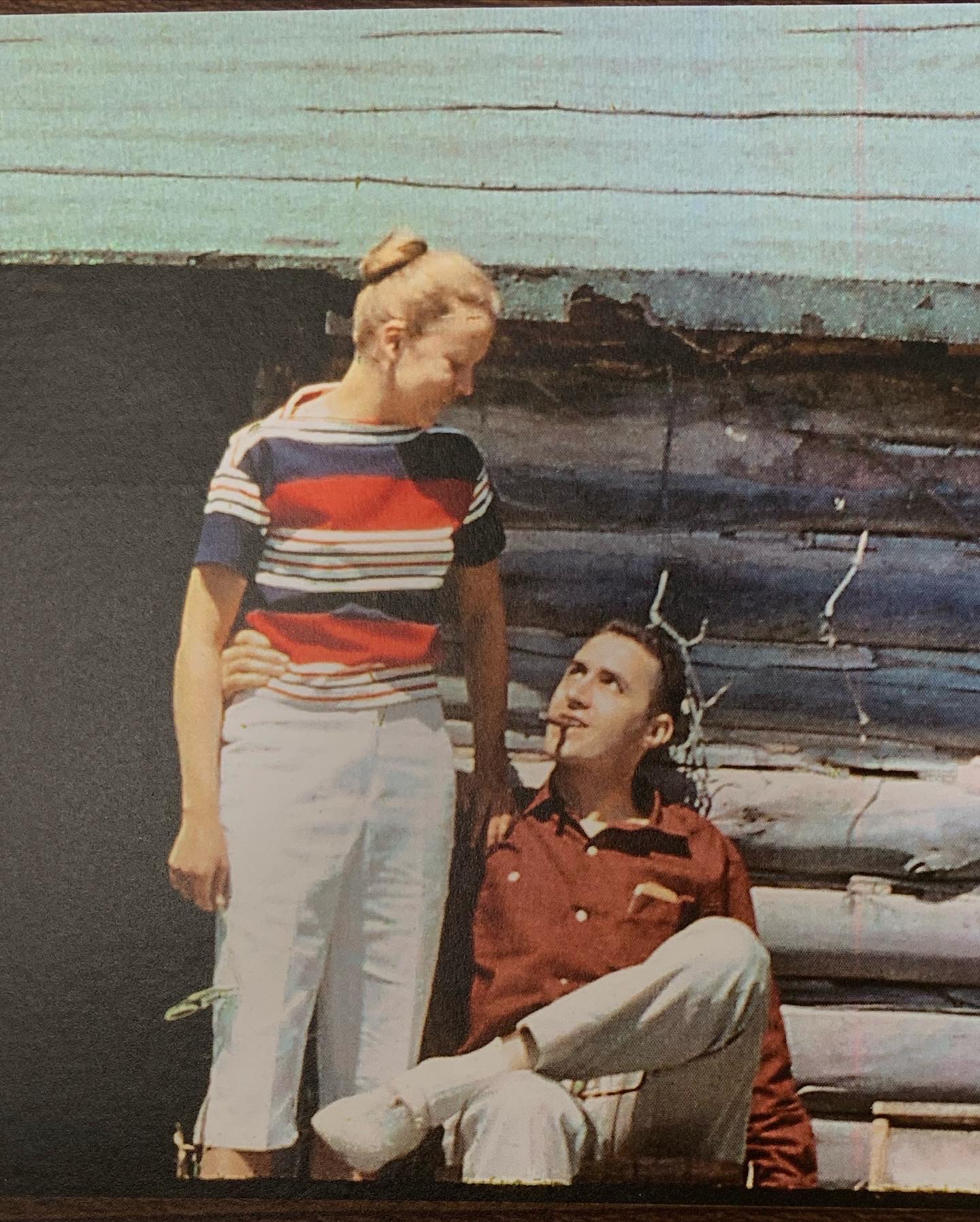 A photo of a man and woman sitting in front of a log cabin.