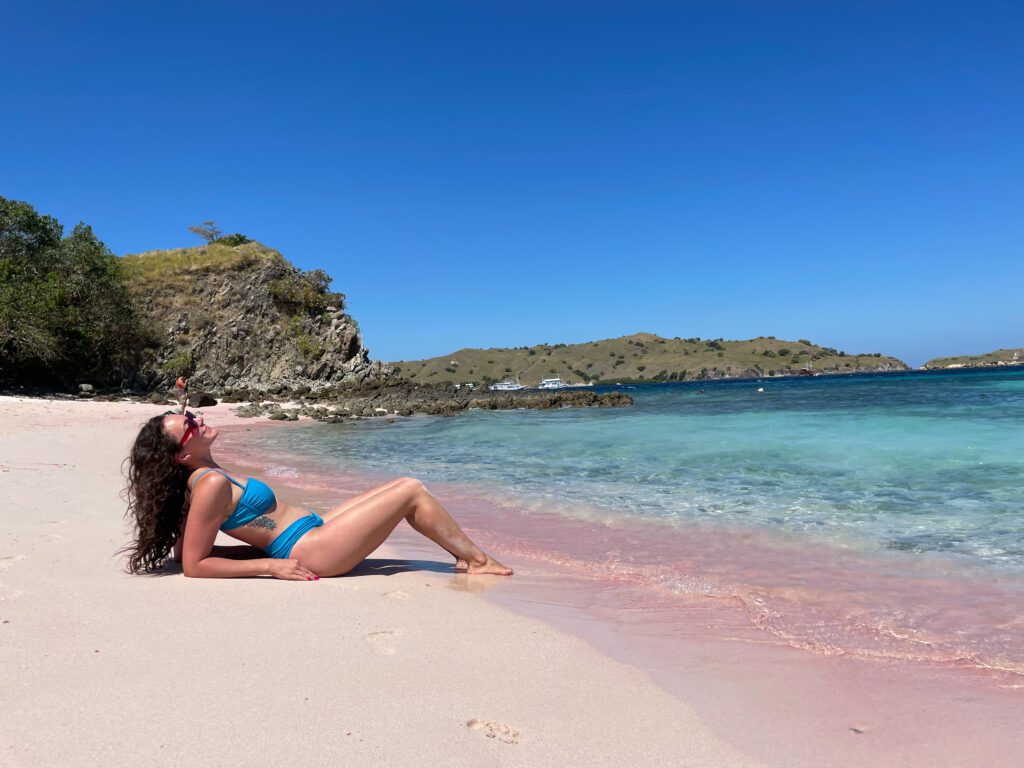 A woman in a bikini laying on a pink sand beach.