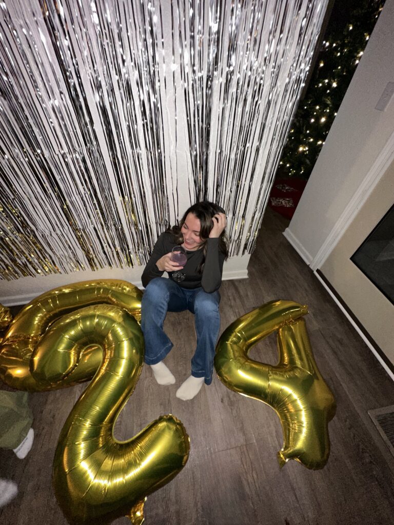 A woman sitting on the floor with gold balloons.