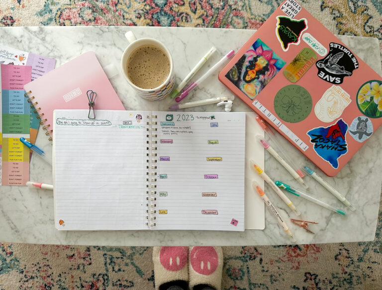 A desk with a notebook, pens, and a cup of coffee.