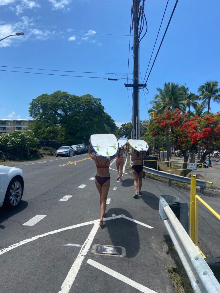 Two women carrying surfboards down a street.