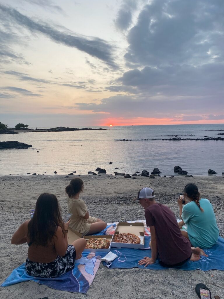 A group of people eating pizza on the beach at sunset.