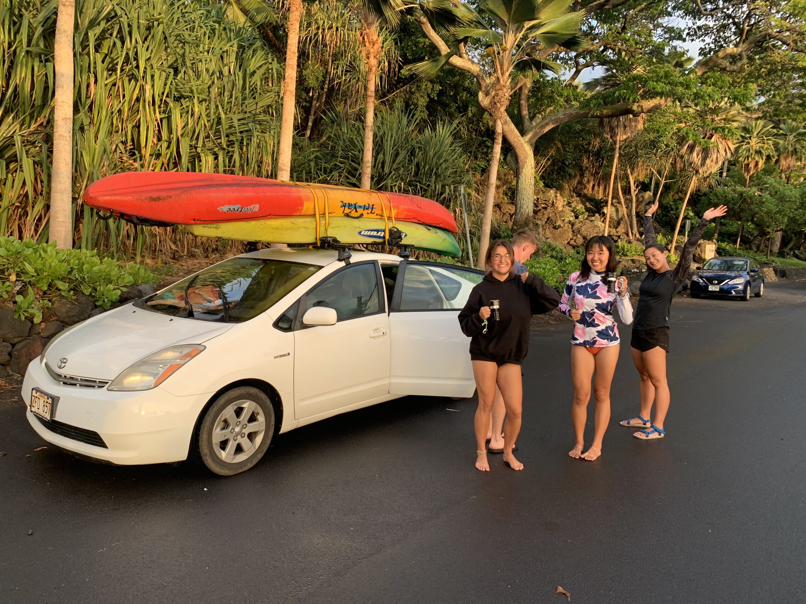 Three girls standing next to a car with kayaks on top.