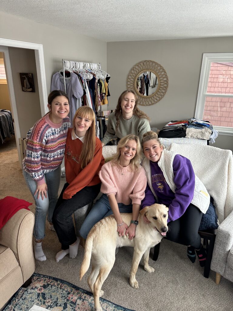 A group of women posing with a dog in a living room.