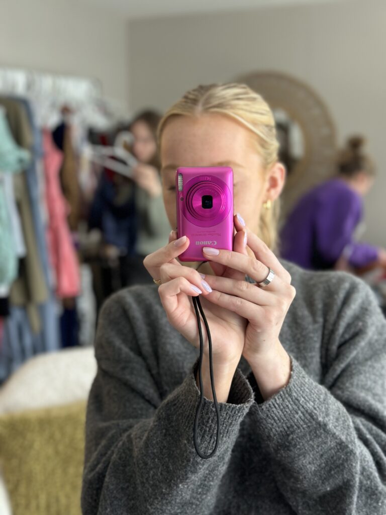 A woman taking a picture with a pink camera.