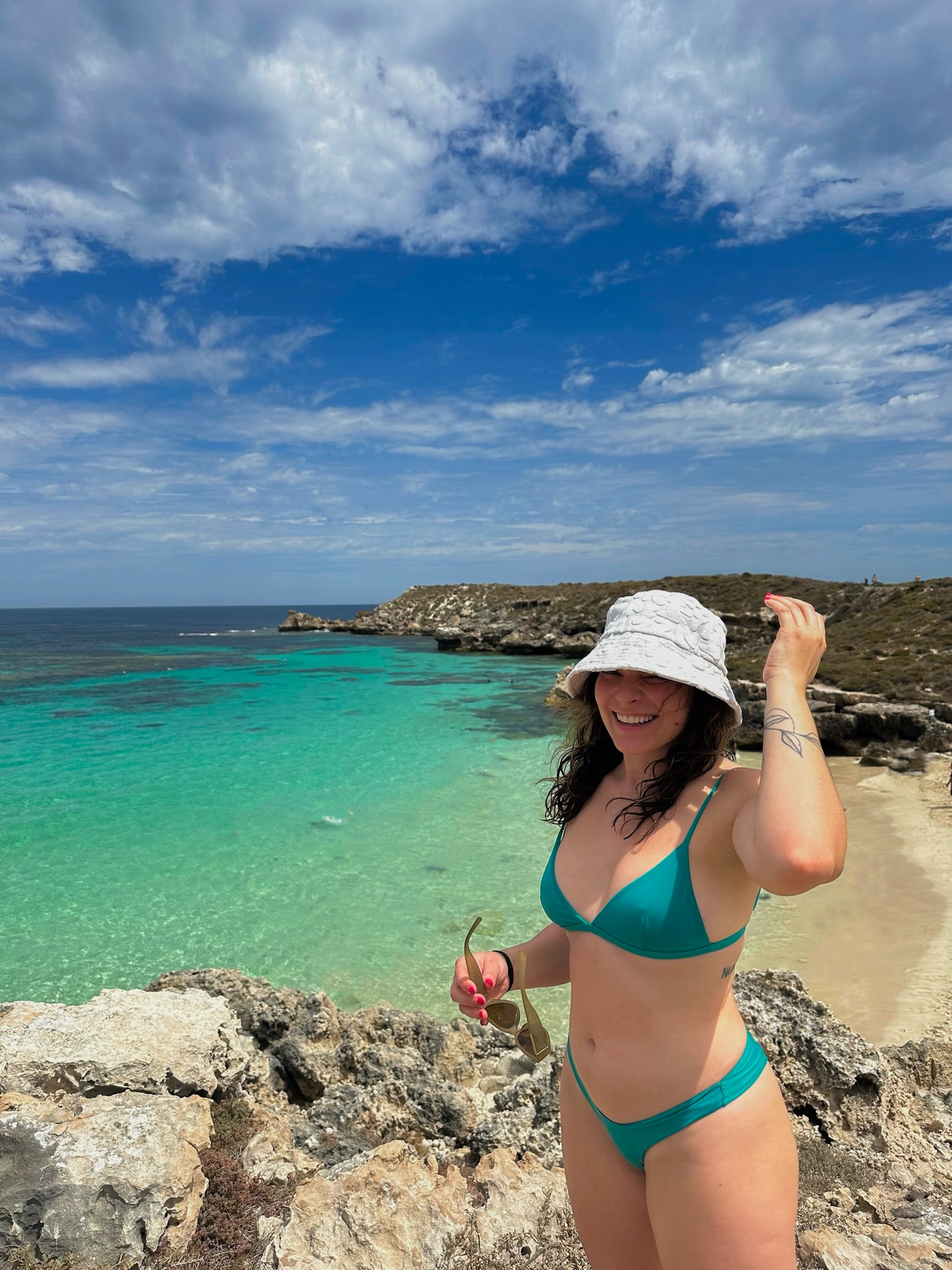 Woman in a bikini enjoying a sunny day at a rocky beach with clear turquoise waters.