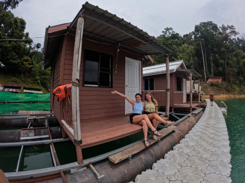 Two people sitting and smiling on the deck of a floating house in Khao Sok National Park, surrounded by forest.